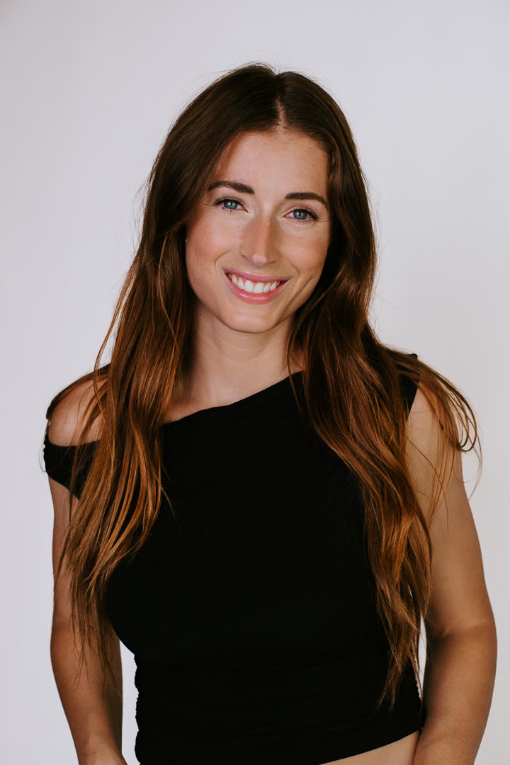Anna smiling in a black top against a light backdrop